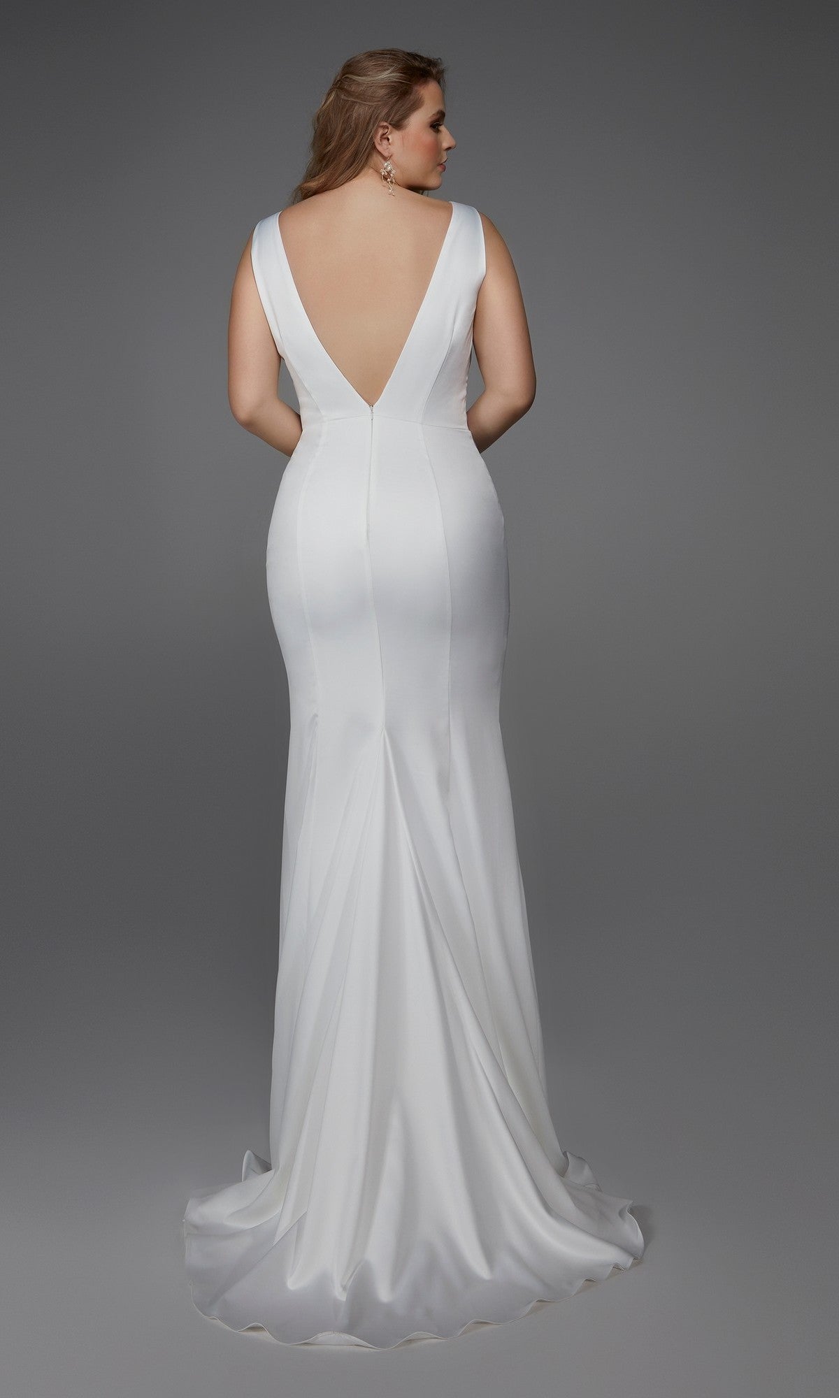 A woman stands with her back to the camera in a sleeveless Long White Dress: Alyce 7019, featuring a deep V-back and floor-length design, against a plain gray background—showcasing its elegant simplicity from behind.